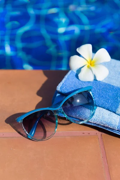 Flauschiges Handtuch mit Sonnenbrille und Blume am Rand eines Schwimmbeckens — Stockfoto