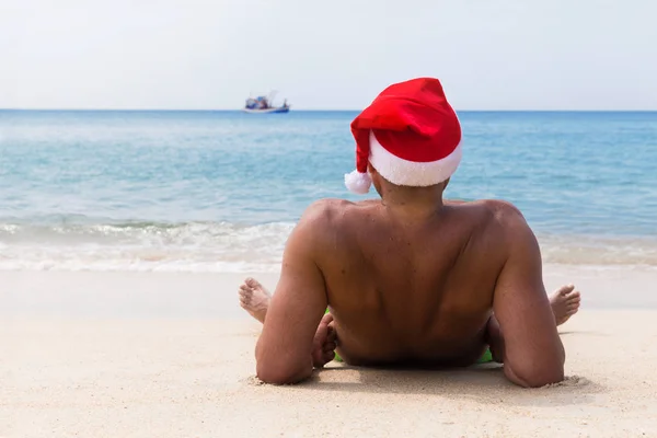 Uomo a Babbo Natale cappello rosso si siede sulla spiaggia in mattinata postumi della sbornia — Foto Stock