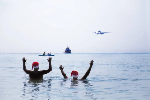 Two men in Santa Claus red hat greet salute airplane in morning