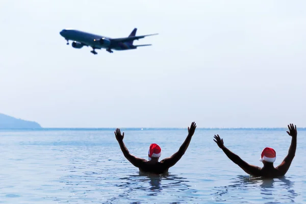 Two men in Santa Claus red hat greet salute airplane in morning