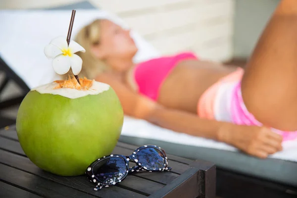 Bebida de suco de coco com mulher na espreguiçadeira perto de uma piscina — Fotografia de Stock