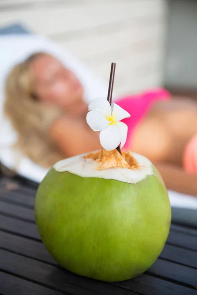 Bebida de suco de coco com mulher na espreguiçadeira perto de uma piscina — Fotografia de Stock