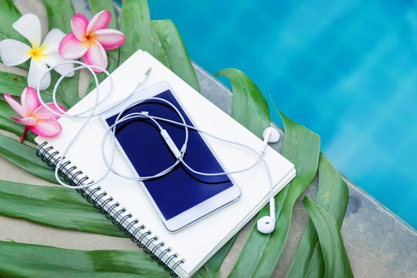 Teléfono inteligente con auriculares, cuaderno de notas, plumeria frangipani flores — Foto de Stock