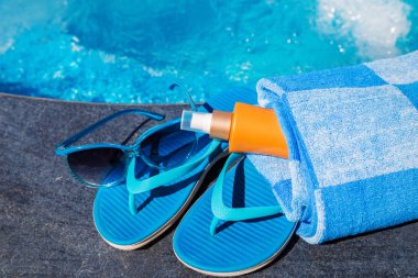 Güneş koruyucu krem, mavi terlik ve havlu bord üzerinde güneş gözlüğü
