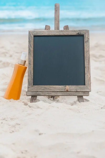 Chalk board with sunscreen cream in the sand on the beach tropic