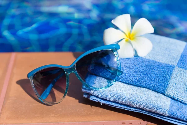 Flauschiges Handtuch mit Sonnenbrille und Blume am Rand eines Schwimmbeckens — Stockfoto