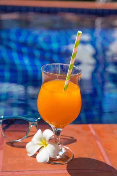 Jugo de naranja con gafas de sol en el borde de la piscina —  Fotos de Stock