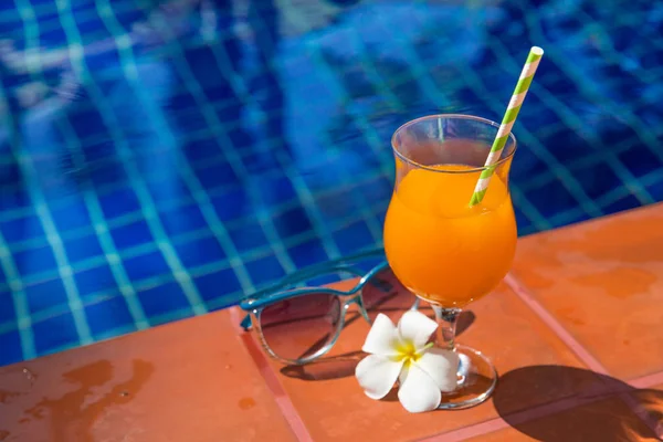 Sumo de laranja com óculos de sol na borda da piscina — Fotografia de Stock