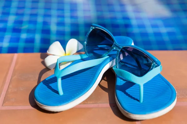 Blaue Hausschuhe und Sonnenbrille am Rand eines Swimmingpools — Stockfoto