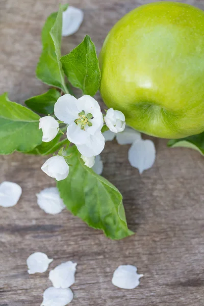 Zelená jablka s květinami na dřevěné pozadí — Stock fotografie