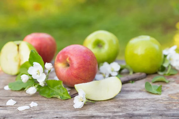 Grön röda äpplen med blommor på trä bakgrund — Stockfoto