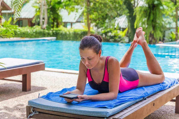 brunette woman read electronic book near pool