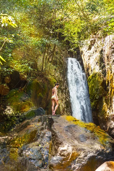 Young woman in a bikini stands on rock waterfall