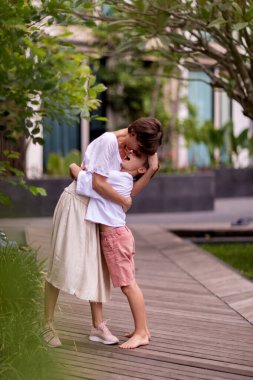 Annesini dışarıda öpen neşeli, genç bir çocuk.