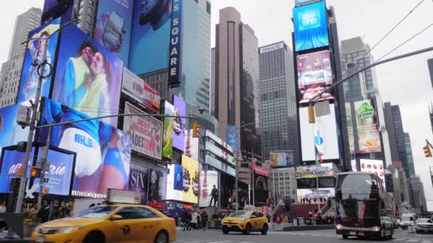 New York, leden 2020 - vozidla včetně taxíků a autobusu projíždějí ulicí New Yorku s lidmi čekajícími na křižovatku silnice na chodníku pod mnoha reklamními billboardy visícími na budovách