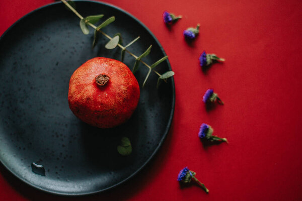 photo of a pomegranate on a black plate with a red background and flowers