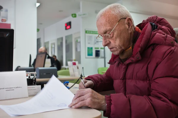 Old man is signing documents at bank — Stock Photo, Image