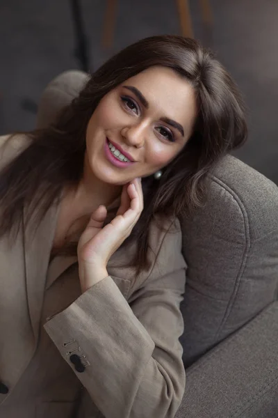 Güzel makyajlı bir kız gülümser ve sandalyeye oturur.