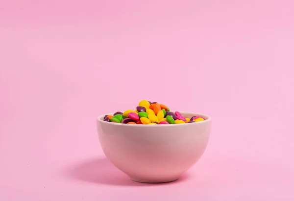 Bowl full of color candies on pink background