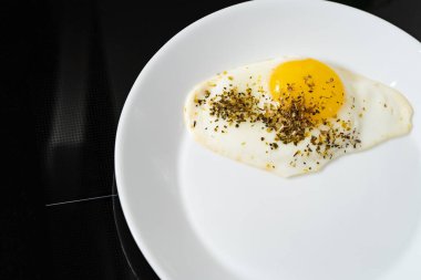 Siyah arka planda beyaz tabakta kızarmış tavuk yumurtası.