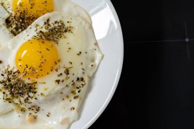Siyah arka planda beyaz tabakta kızarmış tavuk yumurtası.