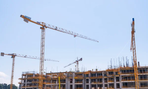 İnşaat halindeki işçilerle birlikte inşaat halindeki bir binanın arka planında vinçler.