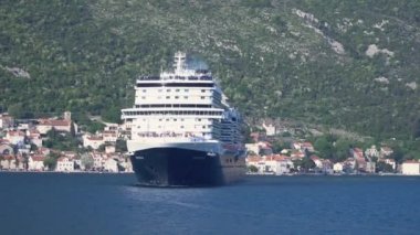 Kotor Montenegro körfezindeki dağların arka planına karşı mavi beyaz büyük bir yolcu gemisi.