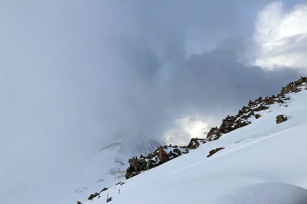 snowy mountain side with stones and birds in the clouds