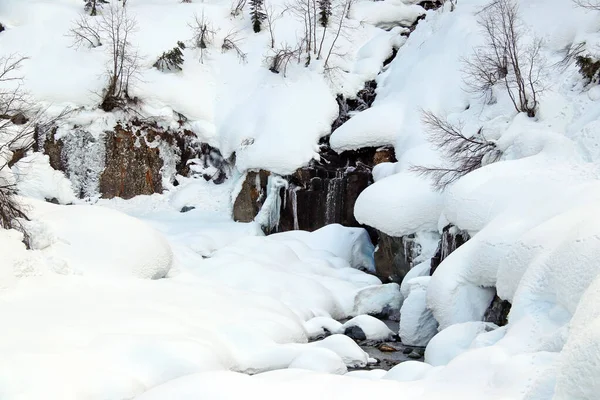 O córrego da montanha flui entre as rochas e a neve branca inchada nas margens — Fotografia de Stock