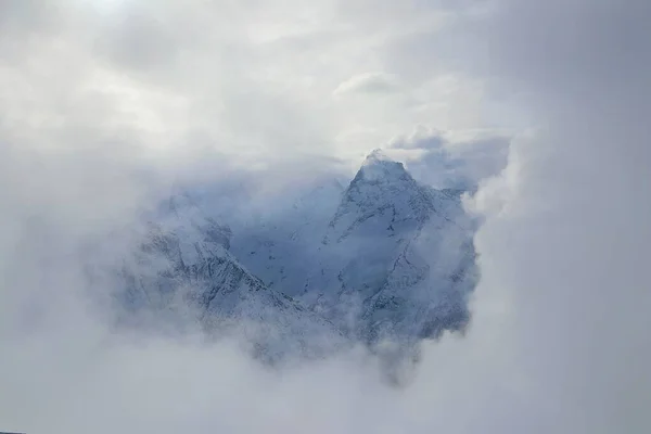 Vista sobre montanhas nevadas pico através de nuvens — Fotografia de Stock