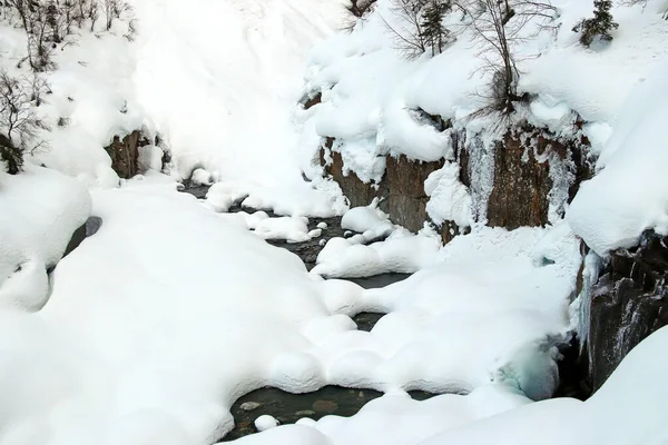 Bergbeekje stroomt tussen de rotsen en gezwollen witte sneeuw op de oevers — Stockfoto