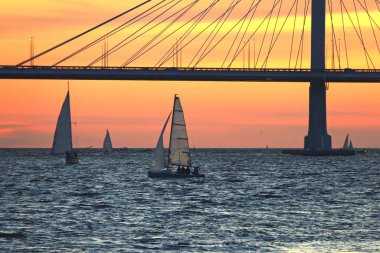 Sahildeki gözlem güvertesinde kablo destekli köprü ve günbatımı manzarası var.