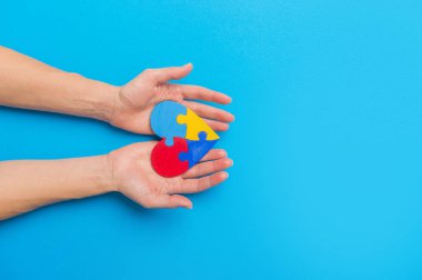 Hand Holding Colorful Heart On Blue Background. World Autism Awareness Day Concept clipart