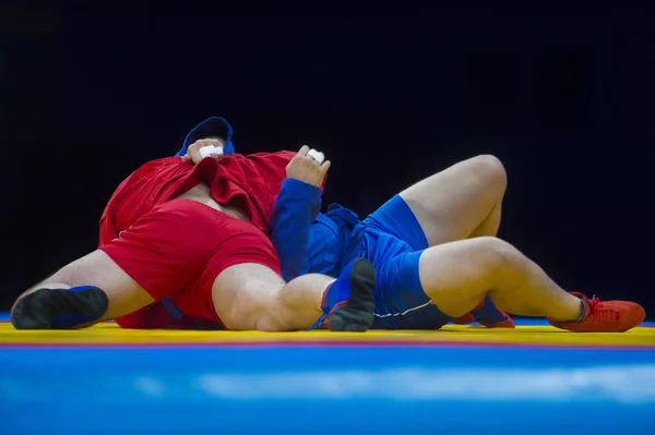 两个穿蓝色和红色摔跤的男人躺在一条黄色摔跤地毯上 — 图库照片