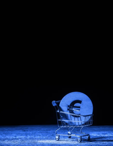 The Euro sign in a supermarket trolley on a wooden table. Business, Finance, currency funds. Blue filter