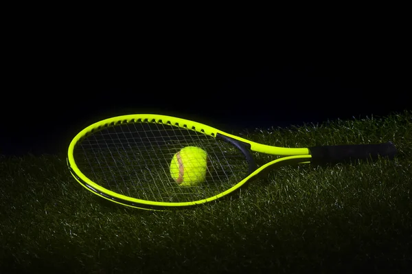 緑のテニスラケット黒の背景とコピースペースと芝生の上で緑の色でテニスボール — ストック写真