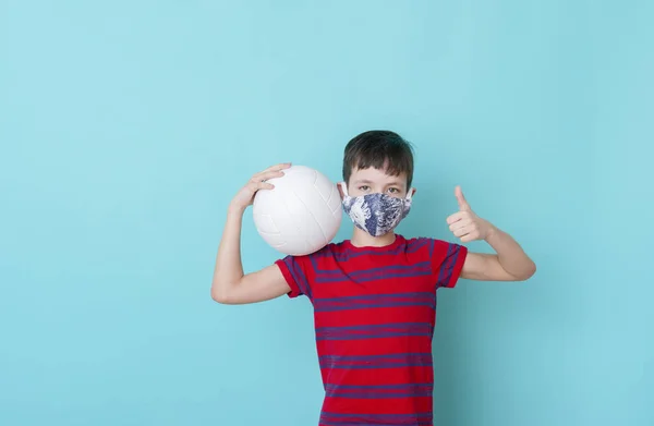 青い背景にコロナウイルスのためのマスクをした少年がボールを再生します ワークアウトオンラインコンセプト — ストック写真