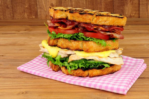 Chicken and bacon double decker sandwich on a wood background