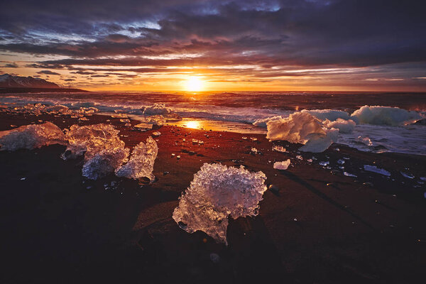 Sunrise at Diamond beach with ices from Jokulsarlon glacier lagoon get washed ashore and strand on the black beach, Iceland