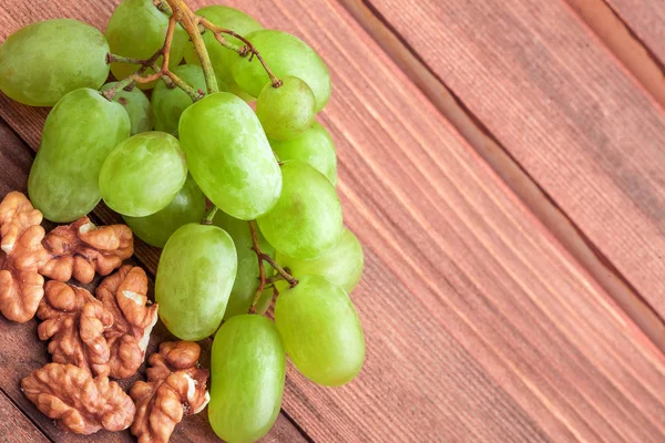 Green grapes and walnut on wooden table.