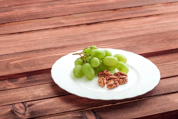 Gröna druvor och valnöt i vit platta på träbord. — Stockfoto