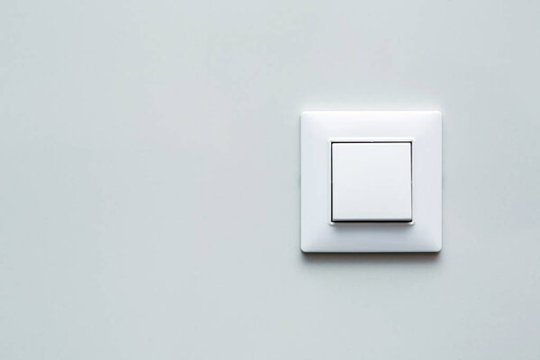 a light switch, a plastic mechanical button of white color installed on a light wall with copy space for text.