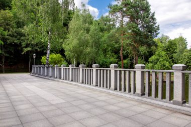 Taştan kiremitleri olan bir köprü manzarası ve arka planda kare sütunları olan granit korkuluklar yeşil ağaçlar ve gökyüzü olan bir park, hiç kimse.