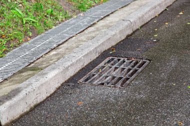 storm systems on an asphalt road a manhole grille behind a curb a drainage system grid after rain. clipart
