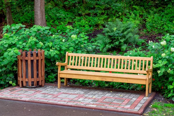 wooden bench with a wooden trash can in the park with green plants on a summer day, nobody.