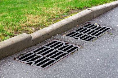 Rögar kapağı yağmuru asfalt bir yolda, yol kenarındaki taş kaldırım kenarındaki yeşil çimlerde rendeleyin..