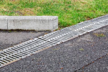 Asfalt yolda demir ızgara drenaj sistemi, yol kenarında kaldırım, yeşil çimenler, yakın çekim..