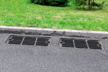 # İki rögar kapağı yağmuru # # asfalt bir yolda # # kaldırımın kenarındaki yeşil çimlerin yanında # # güneşli yaz gününde #.