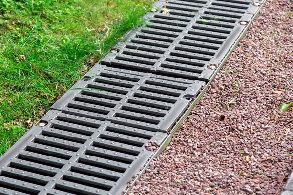 iron grate of a drainage channel on a landscape with pebbles and green grass, closeup detail.