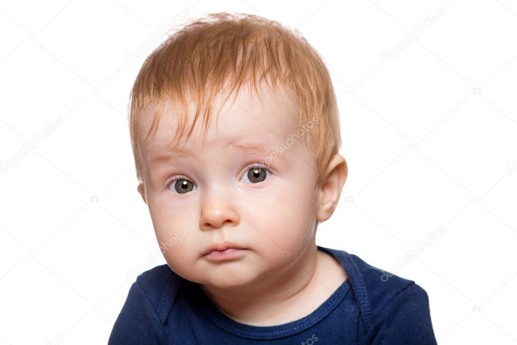 baby boy portrait isolated on white background. the red-haired toddler embarrassedly raised his eyebrows and looks into the frame.
